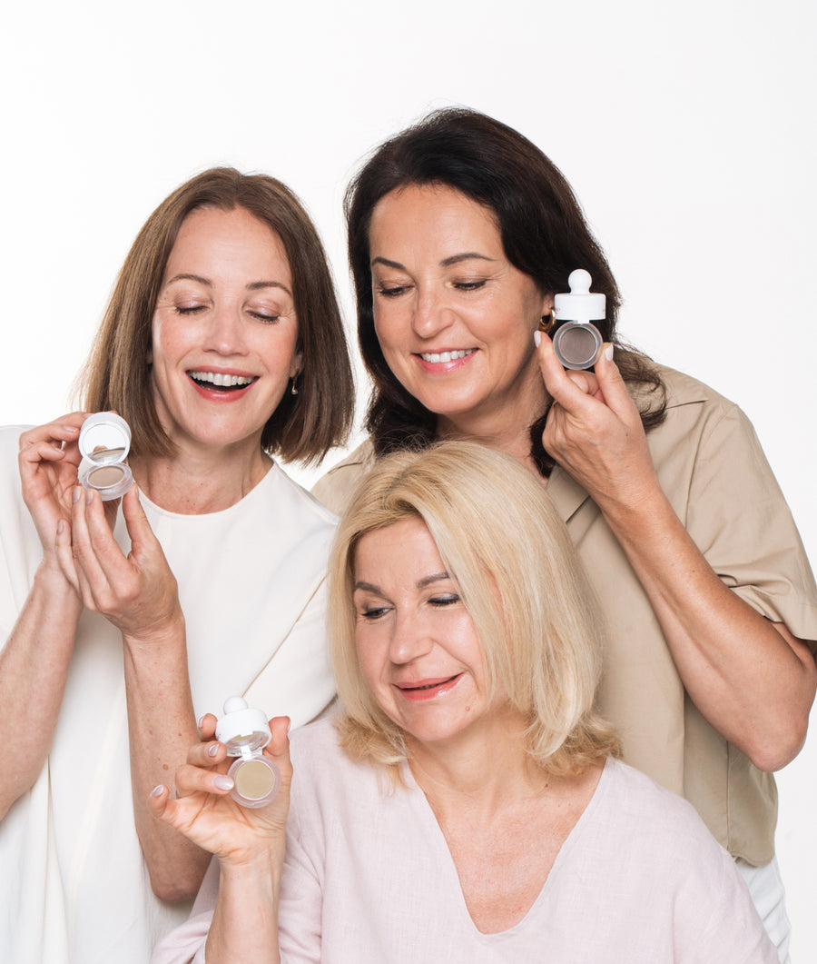 Three women over 50 smiling and holding their HairMagic+ Hairline Powder compacts